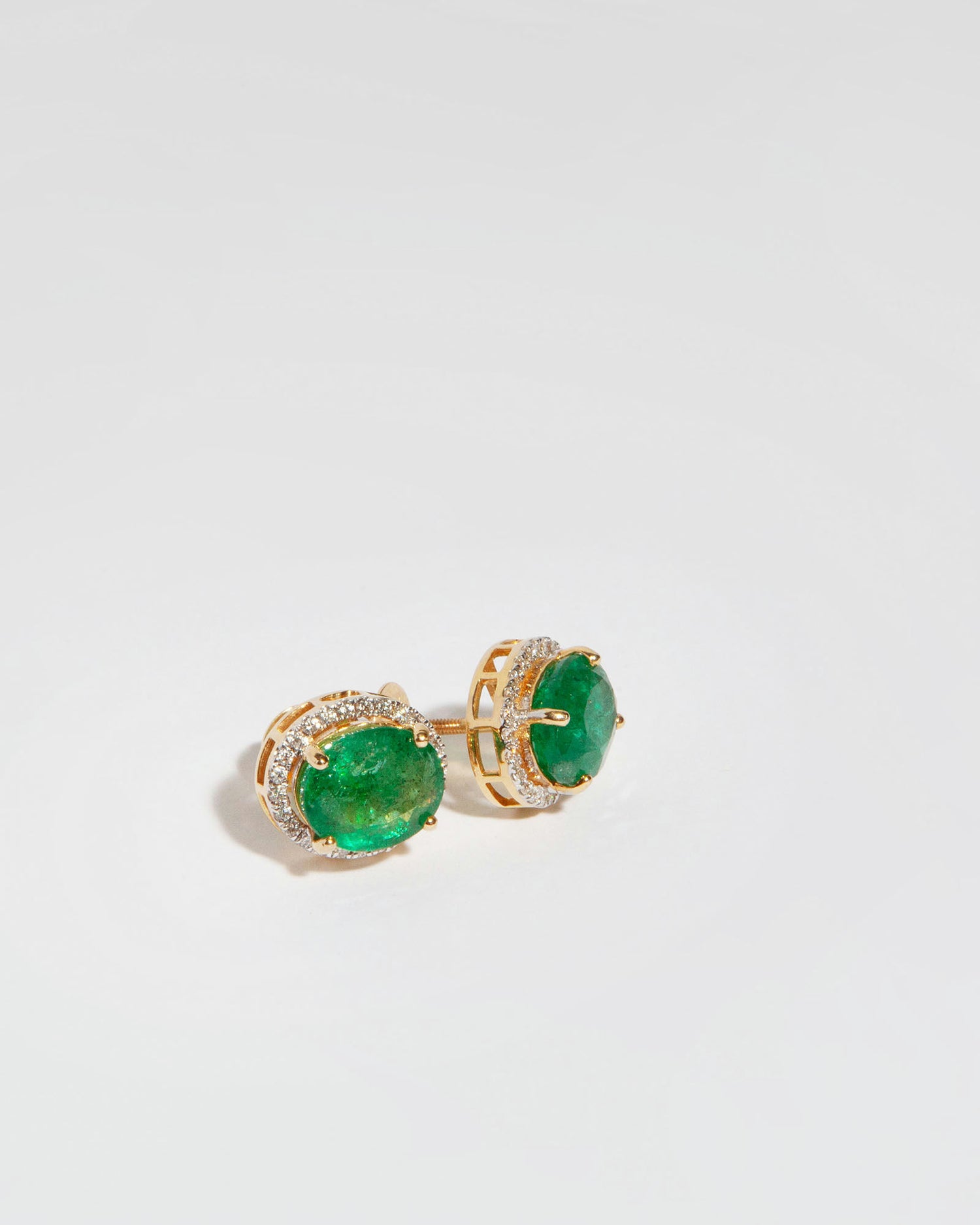 Stud earrings in 14K yellow gold featuring two oval mixed-cut natural emeralds (6.60 ct) and 51 natural diamonds (0.40 ct).